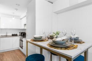 a white kitchen with a table with plates and glasses at Cosy & beautiful home sleeping up to 5 with SmartTV, Free Wifi and Garden in Hemel Hempstead