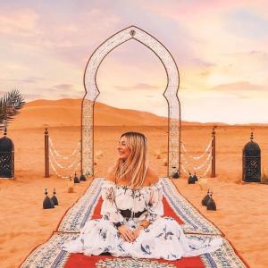 a woman sitting in front of an arch in the desert at Merzouga Desert Luxury Camp in Merzouga
