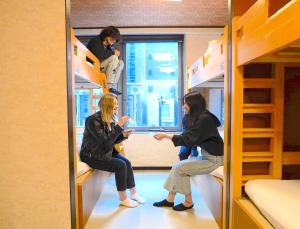 duas mulheres estão sentadas em beliches num quarto em COGO Ryogoku em Tóquio
