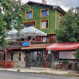 un bâtiment avec une table et des parasols devant lui dans l'établissement Семеен хотел Калина Family hotel Kalina Говедарци, à Govedartsi