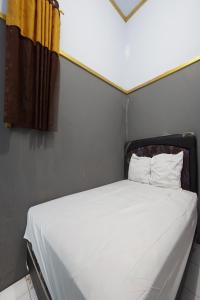 uma cama com lençóis brancos e uma cortina amarela em SPOT ON 93620 Anisa Homestay Syariah em Tulungagung