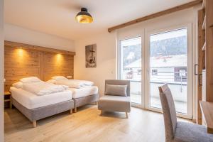 a bedroom with two beds and a chair and a window at Hotel Eschenhof & Apartments in Fulpmes