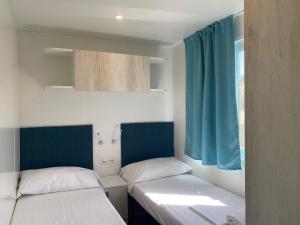 two beds in a small room with blue curtains at Camping Village Il Poggetto in Troghi