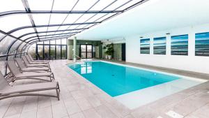 a swimming pool in a building with lounge chairs at Kyriad Prestige Residence & Spa Cabourg-Dives-sur-Mer in Dives-sur-Mer