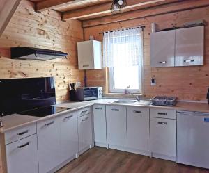 a kitchen with white cabinets and a wooden wall at Domek Na Starej Cegielni in Baligród