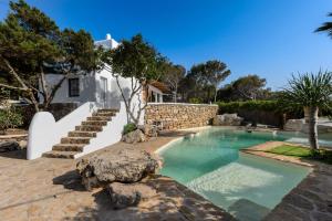 a swimming pool with a stone wall and stairs next to a house at Cala Salada Sunset View in San Antonio