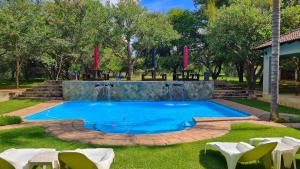 a pool with a waterfall in a park with white chairs at Summerset Place Country House in Bela-Bela