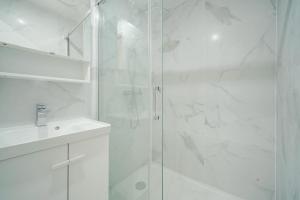 ein weißes Bad mit einer Dusche und einem Waschbecken in der Unterkunft Appartement Mairie des Lilas - III in Les Lilas