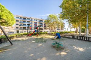 un parc avec une aire de jeux en face d'un bâtiment dans l'établissement HomeHolidaysRentals Fortuny - Costa Barcelona, à Pineda de Mar