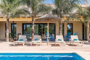 eine Gruppe von Stühlen und einem Sonnenschirm neben einem Pool in der Unterkunft Villa Ca Na Marga in Muro