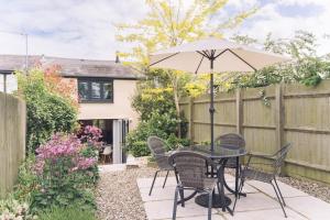 un patio con mesa, sillas y sombrilla en Contemporary mid-terrace cottage, en Priors Marston