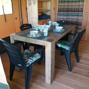 a wooden table and chairs with bowls and plates on it at Boerderijcamping de Berghoeve in Ruinen