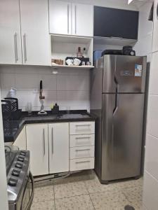 uma cozinha com um frigorífico de aço inoxidável e armários brancos em Duplex pé na areia, praia do Tombo - Guarujá/SP. no Guarujá