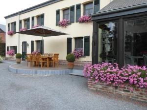 a patio with a table and umbrella and flowers at Le Bien-Aller des Perêts in Saint-Hubert