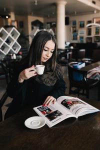 a woman sitting at a table with a book and a cup of coffee at Business Hotel Plovdiv in Plovdiv