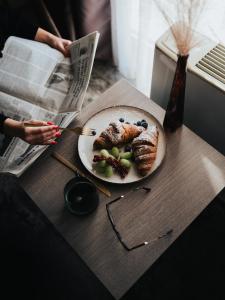 a table with a plate of food and a person reading a newspaper at Business Hotel Plovdiv in Plovdiv