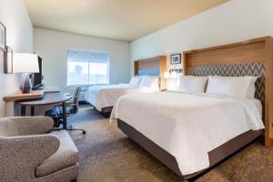 Holiday Inn & Suites Cedar Falls-Waterloo Event Ctr, an IHG Hotel في سيدار فولز: غرفة فندقية بسريرين ومكتب وكرسي