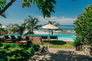 a pool with chairs and an umbrella and the ocean at Puro Surf Hotel & Performance Academy in El Zonte