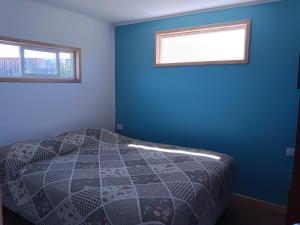 a bedroom with a bed with a blue wall and two windows at Entre Pinos y Volcanes in Frutillar