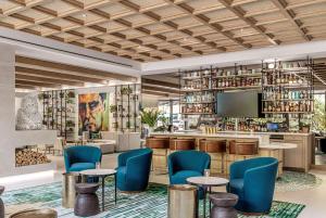 a lobby with a bar with blue chairs and a tv at The Ray Hotel Delray Beach, Curio Collection By Hilton in Delray Beach