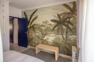 ein Schlafzimmer mit einem Wandbild von Palmen und einer Bank in der Unterkunft Apartamento acolhedor em Lagos in Lagos