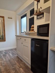 una cucina con armadietti bianchi e lavastoviglie nera di The Little Annex a Horsham
