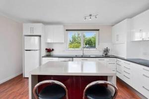 a kitchen with white cabinets and a kitchen island with two chairs at The Baker's Cottage in the Heart of Richmond Sleeps 6 in Hobart