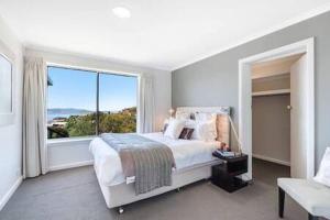 a white bedroom with a bed and a large window at House on the Hill with a View-Sleeps 12 in Hobart