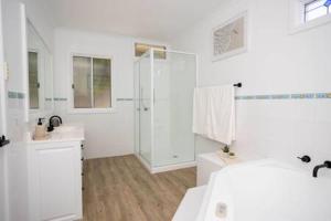 La salle de bains blanche est pourvue d'une douche et d'un lavabo. dans l'établissement River View Holiday House Sleeps 8 10min to CBD, à Hobart