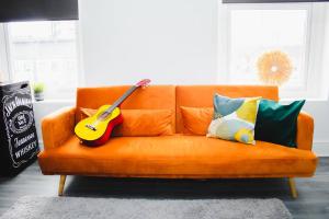 an orange couch with a guitar on it in a living room at Vibrant Studio Close to Anfield Stadium in Liverpool