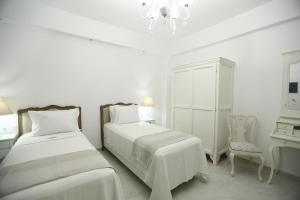 a white bedroom with two beds and a chair at The White Suites in Adamas