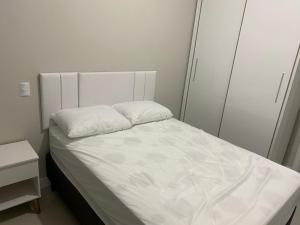 Cette petite chambre comprend un lit avec des draps blancs. dans l'établissement Apartamento com piscina a 100 metros da praia, à Governador Celso Ramos