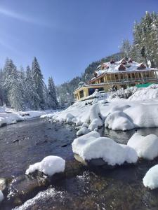 a house with snow on the banks of a river at Shiva Valley Riverside Home Stay in Jibhi
