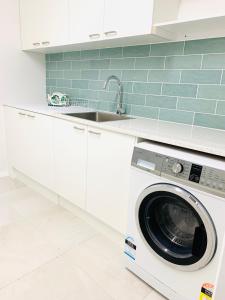 een wasmachine in een witte keuken met een wastafel bij Deluxe Queen Studio Fully Self Contained- Living, kitchenette, laundry, bedroom, bathroom, parking, Wifi, - Free shuttle Service in Gold Coast