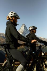 SCHLOSS Zermatt - Active & CBD Spa Hotel في زيرمات: شخصان يركبان الدراجات أمام الجبل