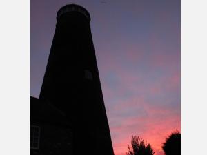 a silhouette of a lighthouse against a sunset at The Old Mill, 7 storey,, dog friendly outdoor pool & bbq in Stoke Ferry