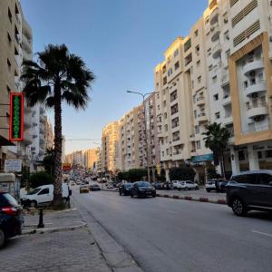 a busy city street with cars and buildings and a palm tree at Spacious Apartment Ennasr 2 in Ariana