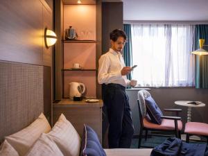 un hombre parado en una habitación de hotel mirando su celular en Mercure Tokyo Ginza, en Tokio