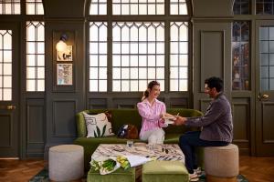 un hombre y una mujer sentados en un sofá estrechando la mano en The Samuel Ryder Hotel St Albans, Tapestry Collection Hilton, en Saint Albans