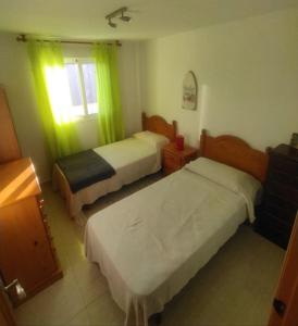 een slaapkamer met 2 bedden en een raam met groene gordijnen bij Piso ideal con piscina y terraza, próximo a playa in Roquetas de Mar