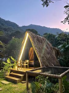 a hut with a grass roof with a table and chairs at ALMAH GLAMPING in Cali