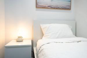 um quarto com uma cama branca e uma mesa de cabeceira com um candeeiro em 2 BD Luxury apartment at heart of Docklands with 85" flat TV & Free Carpark em Melbourne