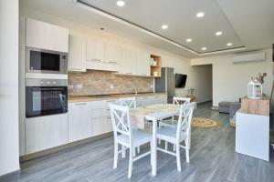セント・ポールズ・ベイにあるTwo Bedroom Apartment in Xemxija, St. Paul's Bayの白いキャビネット、テーブルと椅子付きのキッチンが備わります。
