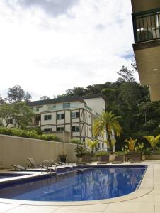 a swimming pool with chairs and a building in the background at Estúdios no Resort Granja Brasil em Itaipava in Petrópolis