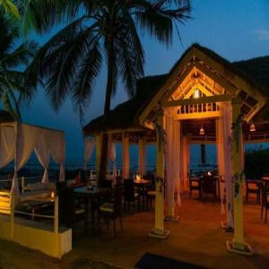 a restaurant with tables and chairs and palm trees at night at zoz Mg in Old Goa