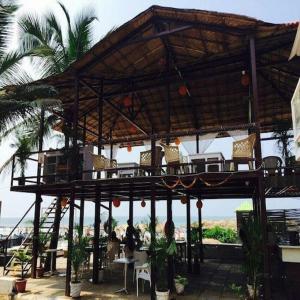 a wooden pavilion with chairs and tables on a beach at zoz Mg in Old Goa