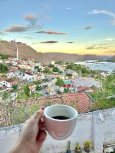 a person holding a cup of coffee on a ledge at Pousada Asa Branca in Piranhas