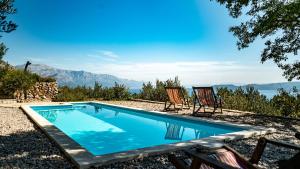 a swimming pool with two chairs and a view of the mountains at Dalmatian stone villa with heated pool in Lokva Rogoznica +36 photos