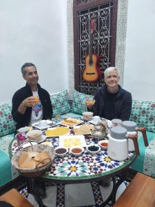 deux hommes assis à une table avec de la nourriture et une guitare dans l'établissement Riad Fes Colors & Spa, à Fès