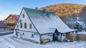 a white house with a green roof in the snow at Górski Sad - Pokoje in Piechowice